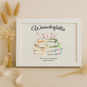 May include: A white frame with a white mat and a black inscription that reads "Wunschersch&uuml;ller". Inside the frame is a birthday cake made of money with candles on top. The text below the cake reads "Alles Gute zum Geburtstag Sabine & Marcus".