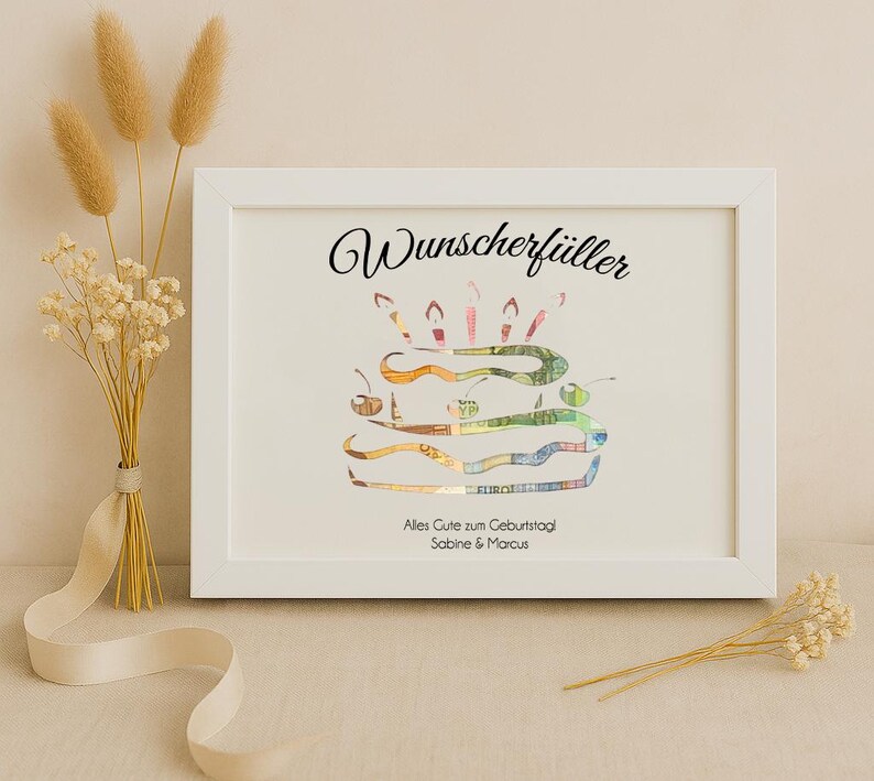 May include: A white frame with a white mat and a black inscription that reads "Wunschersch&uuml;ller". Inside the frame is a birthday cake made of money with candles on top. The text below the cake reads "Alles Gute zum Geburtstag Sabine & Marcus".