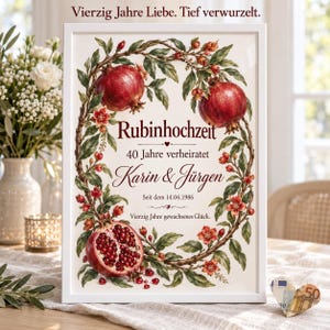 Op de afbeelding: Een ingelijste print met een botanische krans van granaatappels en bladeren rondom de tekst "Rubinhochzeit", "40 Jahre verheiratet", "Karin & Jürgen", "Seit dem 14.06.1986", "Vierzig Jahre gewachsenes Glück" en "Vierzig Jahre Liebe. Tief verwurzelt."