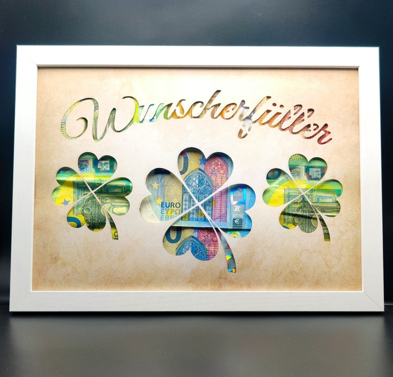 May include: A white frame with a cutout of three shamrocks. The shamrocks are filled with euro bills. The text "Wunschkoffer" is written in the top center of the frame.