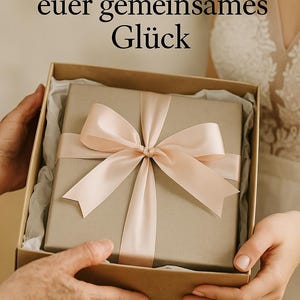 May include: A gift box with a light brown wrapping and a pale pink satin ribbon tied in a bow. The box is held open, revealing the wrapped present inside. Text in German is visible at the top of the image.