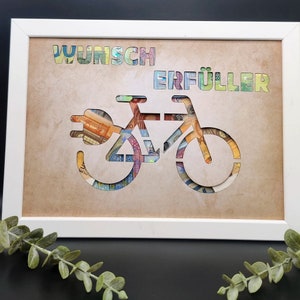 May include: A white frame with a brown background. The frame contains a cutout of a bicycle with a plug on the front. The bicycle is made of euro bills. The words "Wunsch Erf&uuml;ller" are written above the bicycle.