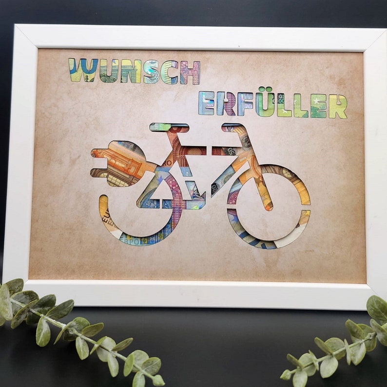 May include: A white frame with a brown background. The frame contains a cutout of a bicycle with a plug on the front. The bicycle is made of euro bills. The words "Wunsch Erf&uuml;ller" are written above the bicycle.