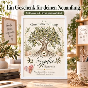 Könnte beinhalten: Ein weiß gerahmter Druck mit einer Olivenbaum-Illustration und dem Text "Zur Geschäftseröffnung", "Sophie", "Ideenreich" sowie "Was du mit Herz beginnst, darf mit dir wachsen." Ein zu einem Herz gefalteter Zehn-Euro-Schein ist unten links befestigt.