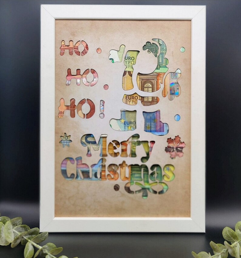 Puede incluir: Una imagen enmarcada en blanco con un fondo beige. La imagen presenta un dise&ntilde;o recortado de un reno con las palabras "&iexcl;Ho Ho Ho! Feliz Navidad" en el fondo. Los recortes est&aacute;n llenos de billetes de euro.
