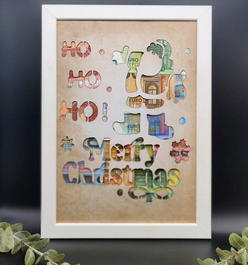 Puede incluir: Una imagen enmarcada en blanco con un fondo beige. La imagen presenta un dise&ntilde;o recortado de un reno con las palabras "&iexcl;Ho Ho Ho! &iexcl;Feliz Navidad!" en una fuente decorativa. Los recortes est&aacute;n llenos de billetes de euro.