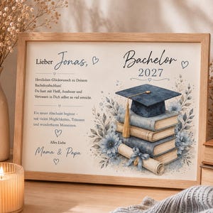 Op de afbeelding: Een ingelijste afstudeerprint met een stapel boeken, een baret en een diploma met blauwe bloemaccenten. De tekst luidt: Lieber Jonas, Bachelor 2027, Herzlichen Glückwunsch zu Deinem Bachelorabschluss! Du hast mit Fleiß, Ausdauer und Vertrauen in Dich selbst so viel erreicht. Ein neuer Abschnitt beginnt - mit vielen Möglichkeiten, Träumen und wunderbaren Momenten. Alles Liebe Mama & Papa.