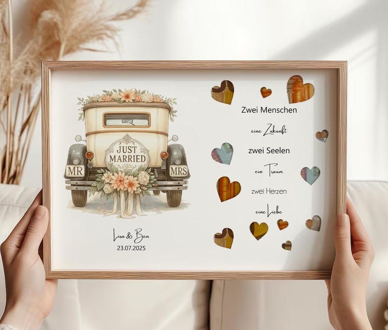 May include: A framed print featuring a vintage car with "Just Married" text, floral accents, and "MR" and "MRS" plates. The print includes text in German and decorative hearts. The names "Lisa & Ben" and the date "23.07.2025" are also present.
