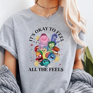 May include: Gray t-shirt with a circular design featuring characters from the movie Inside Out. The text "It's okay to feel all the feels" is printed below the design.