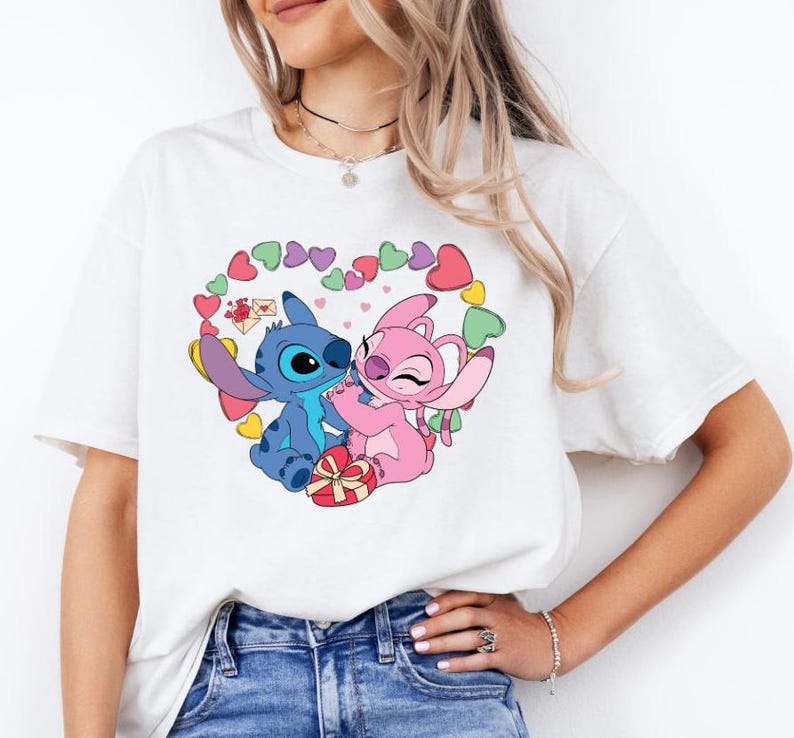 May include: White t-shirt featuring a graphic of Stitch and Angel from Lilo & Stitch. The characters are holding a gift box and surrounded by hearts.