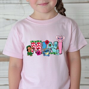 May include: Pink t-shirt with a colorful "MINI" graphic featuring Stitch and other characters from Lilo & Stitch. The letters are decorated with flowers and leaves.
