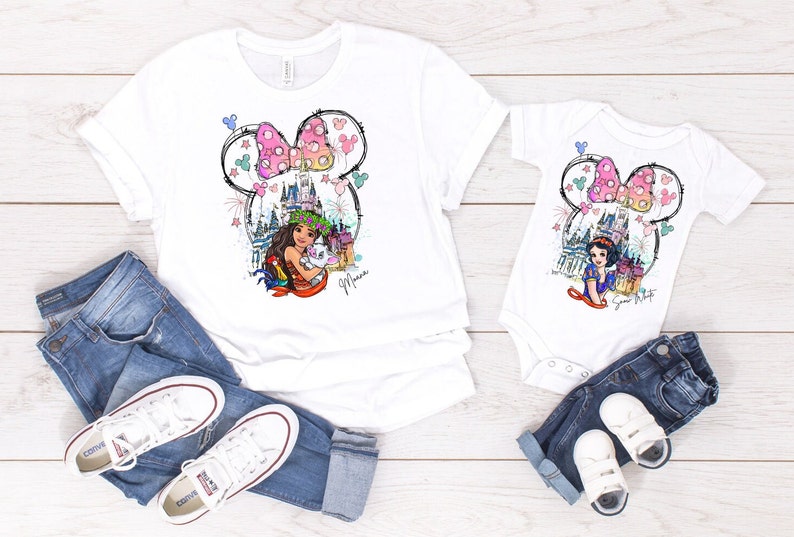 Puede incluir: Camisas blancas con una ilustraci&oacute;n colorida de una princesa de Disney, un castillo y fuegos artificiales dentro de una silueta de oreja de Mickey Mouse. El texto "Mouse" est&aacute; escrito debajo de la ilustraci&oacute;n. Las camisas se combinan con jeans azules y zapatillas blancas.