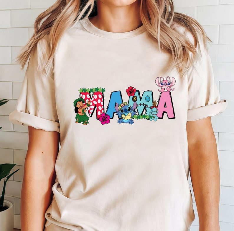 May include: A beige t-shirt with a colorful "MAMA" graphic featuring Stitch and other characters from the Disney movie Lilo & Stitch. The letters are decorated with flowers and leaves.