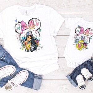 Puede incluir: Una camiseta blanca con un gr&aacute;fico de una princesa de Disney, un castillo y orejas de Mickey Mouse. La camiseta se combina con jeans azules y zapatillas blancas. Tambi&eacute;n se muestra una camiseta blanca m&aacute;s peque&ntilde;a con el mismo gr&aacute;fico.