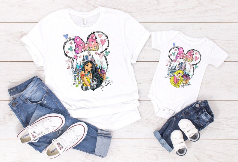 Puede incluir: Una camiseta blanca con un gr&aacute;fico de una princesa de Disney, un castillo y orejas de Mickey Mouse. La camiseta se combina con jeans azules y zapatillas blancas. Tambi&eacute;n se muestra una camiseta blanca m&aacute;s peque&ntilde;a con el mismo gr&aacute;fico.