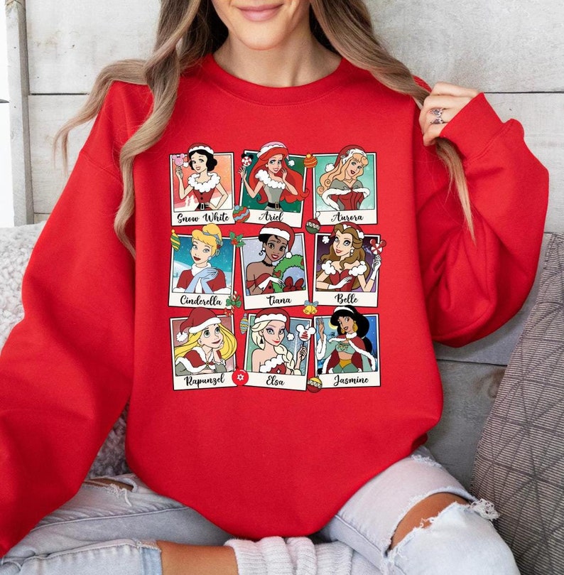 Puede incluir: Sudadera roja con un dise&ntilde;o navide&ntilde;o con nueve princesas Disney con gorros de Pap&aacute; Noel. Las princesas incluyen Blancanieves, Ariel, Aurora, Cenicienta, Tiana, Bella, Rapunzel, Elsa y Jasmine.