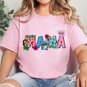 May include: Pink t-shirt with a colorful "MAMA" graphic featuring Stitch and other characters from the Disney movie Lilo & Stitch. The graphic includes flowers and polka dots.