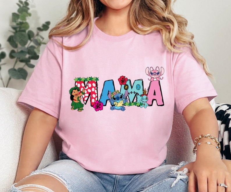 May include: Pink t-shirt with a colorful "MAMA" graphic featuring Stitch and other characters from the Disney movie Lilo & Stitch. The graphic includes flowers and polka dots.