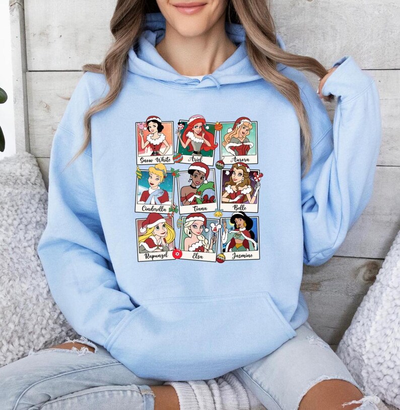 Puede incluir: Sudadera con capucha azul claro con un estampado gr&aacute;fico de nueve princesas Disney con gorros de Pap&aacute; Noel. Las princesas son Blancanieves, Ariel, Aurora, Cenicienta, Tiana, Bella, Rapunzel, Elsa y Jasmine.