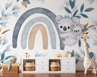 Könnte beinhalten: Ein Wandbild für das Kinderzimmer mit einem Aquarell-Regenbogen in Blau- und Beigetönen, mit einem Mutter- und Baby-Koala. Dekorative Blätter und ein Giraffen-Spielzeug sind ebenfalls vorhanden. Ein weißes Aufbewahrungsmöbel mit Körben und Spielzeug vervollständigt die Szene.