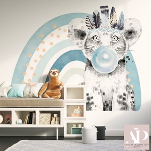 Puede incluir: Un peque&ntilde;o le&oacute;n blanco y gris con un tocado de plumas sopla una burbuja azul frente a un arco&iacute;ris azul y blanco con lunares naranjas. El le&oacute;n es una calcoman&iacute;a de pared.