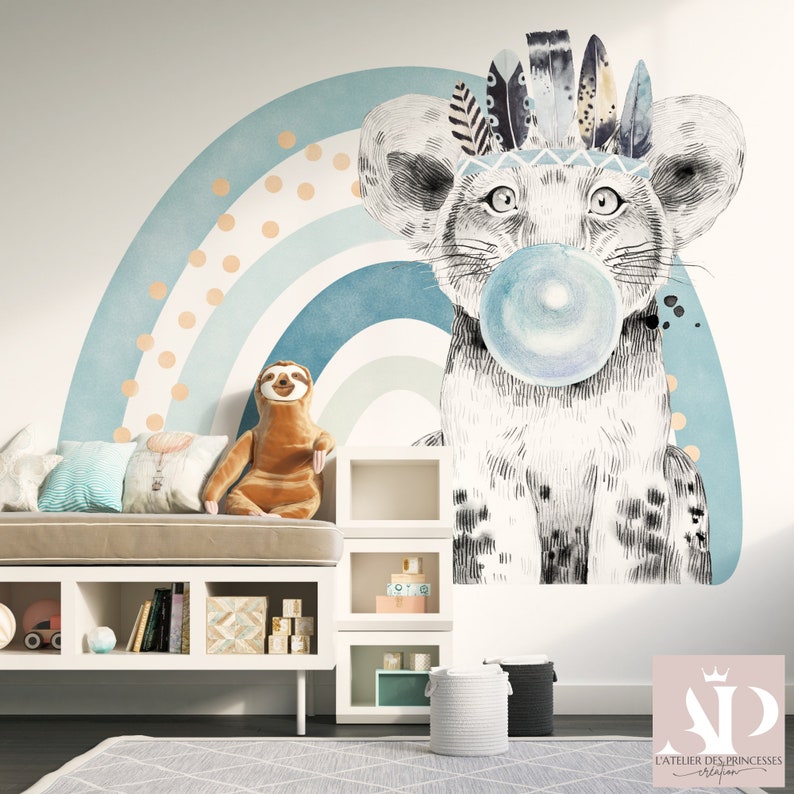 Puede incluir: Un peque&ntilde;o le&oacute;n blanco y gris con un tocado de plumas sopla una burbuja azul frente a un arco&iacute;ris azul y blanco con lunares naranjas. El le&oacute;n es una calcoman&iacute;a de pared.