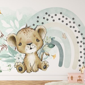 May include: A cute cartoon lion cub sitting in a field of green leaves and flowers. A blue, green, and beige rainbow with black polka dots is in the background.