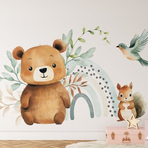 May include: Watercolor wall decal featuring a brown bear, a squirrel, a blue bird, and a rainbow with a white background. The decal is perfect for a nursery or child's room.