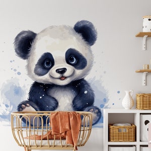 May include: A watercolor illustration of a cute panda bear with black and white fur, sitting in a crib with a brown blanket. The background is a light blue watercolor wash.