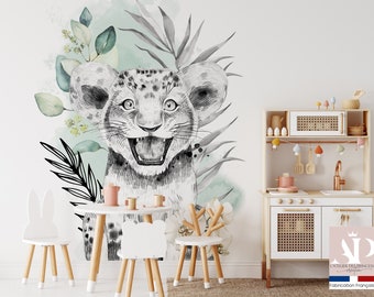 Könnte beinhalten: Ein Wandtattoo für das Kinderzimmer mit einer Illustration eines lächelnden Löwenjungen, Aquarellblättern und einem hellgrünen Hintergrund. Der Raum umfasst einen kleinen weißen Tisch, Stühle und eine Spielküche aus Holz. Der Text "L'ATELIER DES PRINCESSES création" ist sichtbar.