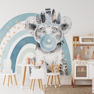 Puede incluir: Una cocina de juguete blanca con una encimera de madera y un armario blanco con una puerta de rat&aacute;n tejido. La cocina tiene un fregadero, una placa de cocci&oacute;n y un horno peque&ntilde;o. Hay decoraciones coloridas colgadas sobre la cocina. Una silla blanca de conejo y una silla blanca de ciervo est&aacute;n frente a la cocina. Un arco&iacute;ris azul y verde con lunares naranjas est&aacute; en la pared detr&aacute;s de la cocina.