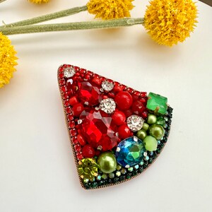 May include: A red, green, and white watermelon-shaped brooch made of beads and rhinestones.