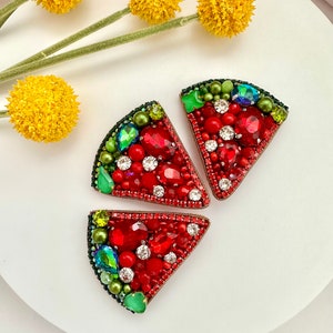 May include: Three watermelon slice shaped brooches made of red, green, and clear rhinestones.