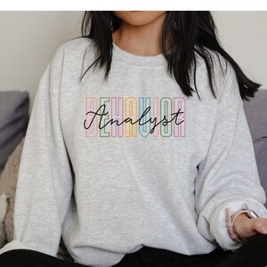 May include: A gray sweatshirt with the text "Behavior Analyst" in rainbow colors.
