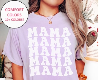 May include: A lavender t-shirt with the word "MAMA" repeated five times in a retro font. The shirt is made of a soft, comfortable fabric and is available in a variety of colors.