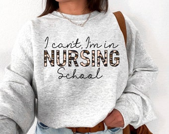 May include: A gray sweatshirt with the text "I can't, I'm in NURSING School" printed on it. The word "NURSING" is in a leopard print pattern.