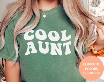 May include: A light green t-shirt with the text "COOL AUNT" in white, retro-style lettering. The shirt is made of a soft, comfortable fabric and is available in a variety of colors.