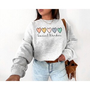 May include: A gray sweatshirt with a row of five colorful hearts and the text "Social Worker" printed on the front.
