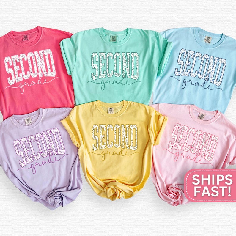 May include: A collection of six colorful t-shirts in pink, mint green, light blue, lavender, yellow, and light pink. Each shirt features the words "SECOND grade" in a white, floral-filled design.