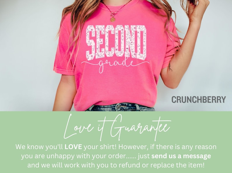 May include: A bright pink t-shirt with the words "SECOND grade" in a white floral design. The shirt is a crew neck style and is made of a soft material. The brand name "CRUNCHBERRY" is printed on the bottom right.