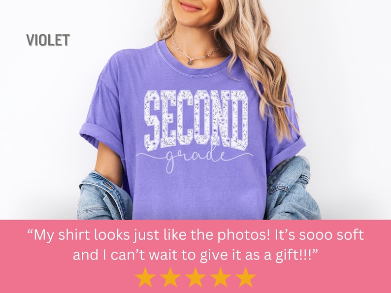 May include: A violet-colored t-shirt with the words "SECOND grade" in white, floral-filled letters. The shirt has rolled-up sleeves and is being worn. The word "VIOLET" is in the upper left corner.