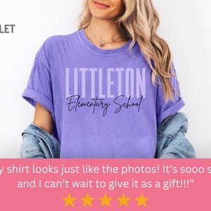 May include: A violet t-shirt featuring the text "LITTLETON Elementary School". The shirt has rolled-up sleeves and is worn by a person. The word "VIOLET" is in the top left corner. The shirt is a shade of purple.