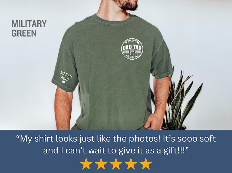 以下が含まれることがあります： 胸に「DAD TAX」の文字が円形にデザインされたミリタリーグリーンのTシャツ。左袖には「MEGAN ADDI」の名前とハートマークが入っています。シャツは無地で、ゆったりとしたフィット感です。