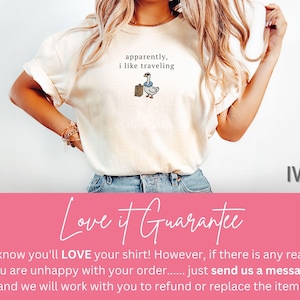 May include: Ivory-colored t-shirt with the text "apparently, I like traveling" above a cartoon goose with a suitcase. The shirt is a light cream color and has a relaxed fit.