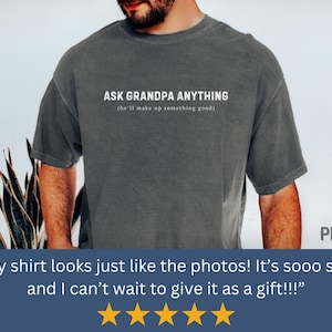 May include: Dark gray t-shirt with the text "ASK GRANDPA ANYTHING" in white, with the phrase "(he'll make up something good)" underneath. The shirt is a casual style, suitable for everyday wear.
