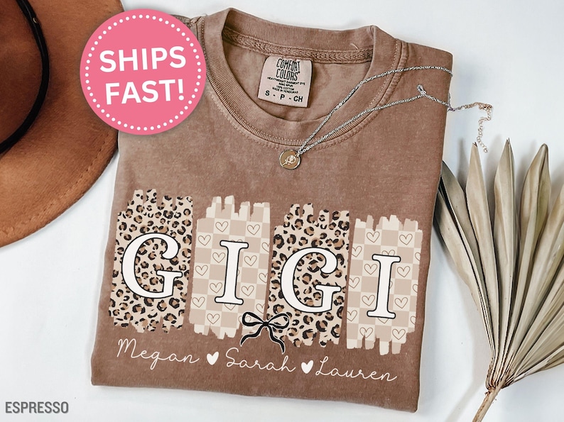 Pode incluir: Camiseta cor espresso com a palavra "GIGI" em um design &uacute;nico. As letras est&atilde;o em um fundo de estampa de leopardo e xadrez. Os nomes Megan, Sarah e Lauren s&atilde;o impressos abaixo. Um c&iacute;rculo rosa com "SHIPS FAST!" &eacute; vis&iacute;vel.