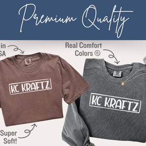 May include: Two t-shirts, one brown and one gray, with the text "KC KRAFTZ" in a white rectangle. The brown shirt is short-sleeved, and the gray shirt is long-sleeved. The image includes the text "Printed in the USA", "Real Comfort Colors", and "Super Soft!"
