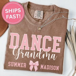 May include: A brown t-shirt with the text "DANCE Grandma" in pink and white lettering. The text "SUMMER" and "MADISON" are also printed on the shirt in white. A pink bow is printed below the text.