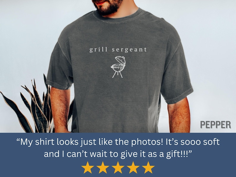 Op de afbeelding: Donkergrijs t-shirt met de tekst "grill sergeant" en een witte afbeelding van een grill. Een casual shirt voor liefhebbers van barbecue&euml;n.