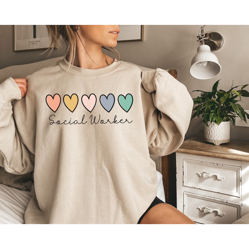 May include: A beige sweatshirt with a row of five colorful hearts and the text "Social Worker" in cursive.